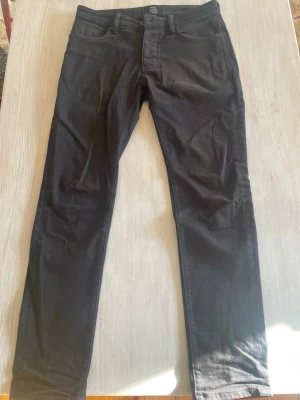 Svarta jeans från Neuw - Snygga svarta jeans från Neuw med klassisk femficksdesign och knappgylf. De har passform regular slim så mitt emellan de. Jeansen har en smal passform och är tillverkade i ett mjukt och material som sitter skönt hela dagen. Perfekta för dig som gillar en stilren och modern look.