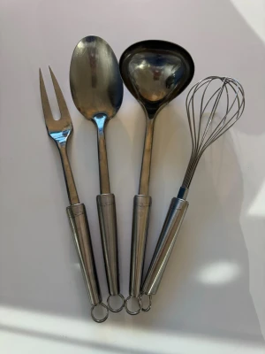 Set med köksredskap i rostfritt stål - Säljer ett set med fyra köksredskap i rostfritt stål från Ander Petter: en visp, en soppslev, en serveringssked och en gaffel. Alla har praktiska öglor för upphängning och ett stilrent, modernt utseende. Perfekt för matlagning och bakning.