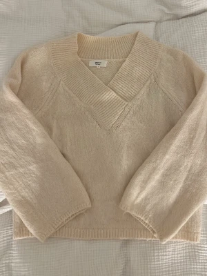 Beige stickad tröja från Gina  - Mysig beige stickad tröja från Gina trixig  med bred ribbad V-ringning och långa ärmar. Tröjan har en avslappnad passform och ribbade muddar vid ärmslut och nederkant. St S. Använd några gånger men är i väldigt fint skick💛