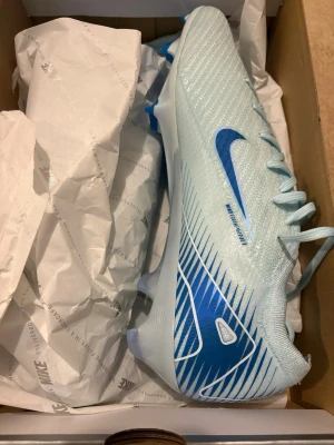Nike Mercurial Vapor Elite 16 - Snygga Nike Mercurial Vapor Elite fotbollsskor i ljusblått med blå detaljer och klassisk Nike-logga på sidan. Skorna har en strömlinjeformad design, snörning och ovandel i syntetmaterial för bra bollkontroll och grepp på planen. Perfekta för dig som vill sticka ut på fotbollsplanen. Väska ingår. 