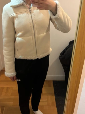 Krämvit pälsjacka med dragkedja - Damjacka - Vändbar jacka i fuskpäls från Tiger of Sweden. CLIMB. - Normal passform - Dragkedja - Öppna sidofickor - Teddyfoder på ena sidan och mockaimitation på den andra - Vändbar dragkedja 