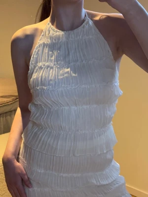 Halterneck topp - Säljer en vit halterneck topp med plisserade detaljer och smockad struktur. Toppen är ärmlös och har en hög halsringning som knyts i nacken - öppen i ryggen! 💕🌸.Perfekt för dig som gillar en stilren och trendig look - perfekt till både vardags och sommarens festligheter! 💕💕🎀☀️