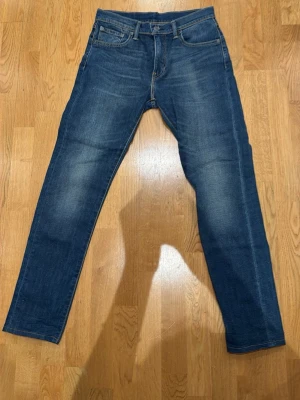 Levi's 512 slim jeans blå - Säljer ett par Levi's 512 slim jeans i klassisk blå denim. Jeansen har fem fickor, normalhög midja och smal passform hela vägen ner. Snygga slitningar och tvättade detaljer ger en cool look. Perfekta för dig som gillar stilrena och tidlösa jeans.