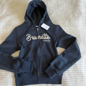 Mörkblå hoodie Brunette Forever från Subdued - Mörkblå hoodie med dragkedja och texten 'Brunette Forever'. Tillverkad i mjukt bomullsmaterial från Subdued. Aldrig använt, lappen kvar. Passar även S