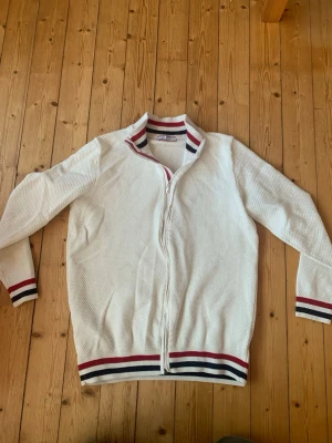Vit ziptröja Felix Hardy  - Använd 2 gånger!!!(Blir som en cardigan) Snygg vit ziptröja från Felix Hardy med ribbade muddar och krage i vitt, rött och marinblått. Tröjan har ett diskret strukturmönster och dragkedja framtill. Perfekt till jeans eller chinos för en clean look.