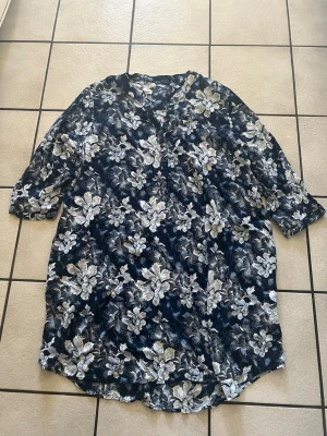 Blommig marinblå klänning med v-ringning - Snygg marinblå klänning med vitblommigt mönster och v-ringad hals. Klänningen har trekvartsärm och avslappnad passform, perfekt för dig som gillar en chill och stilren look. Materialet känns lätt och luftigt, vilket gör den skön att bära under varmare dagar.