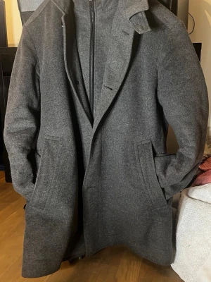 Mörkgrå jacka från Hugo Boss i kaschmir - Snygg mörkgrå kashmirrock från Hugo Boss.   Rocken har knäppning framtill, två sidofickor och en innerdel med dragkedja för extra värme. Perfekt för kyliga dagar och ger en clean look. Nypris: 6300kr. Mitt pris: 1500kr. Storlek M/L