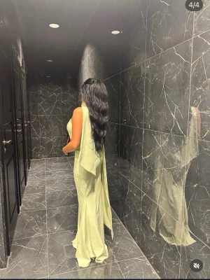 Ljusgrön långklänning med cape / oh polly - Elegant ljusgrön långklänning med axelbandslös design och cape-liknande tygdetalj som faller från axeln. Klänningen har en figurnära passform och är tillverkad i ett glansigt material som ger en lyxig känsla. Perfekt för speciella tillfällen.