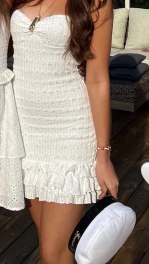 Vit kort volangklänning, Missguided - Supersöt vit kort klänning med smockat tyg och volangdetaljer längst ner. Klänningen är ärmlös och har en figurnära passform som framhäver siluetten. Perfekt för sommarens alla tillfällen!