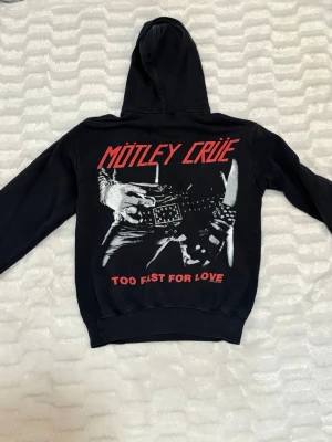 Mötley Crüe hoodie  - Svart hoodie med stor huva och framficka,  med rött Mötley Crüe-tryck. Storlek S