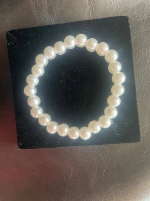 Klassiskt pärlarmband i vitt - Säljer ett stilrent armband med vita, runda pärlor trädda på elastisk tråd. Perfekt för dig som gillar tidlös och elegant stil. Armbandet har en enkel design som gör det lätt att matcha med andra smycken.