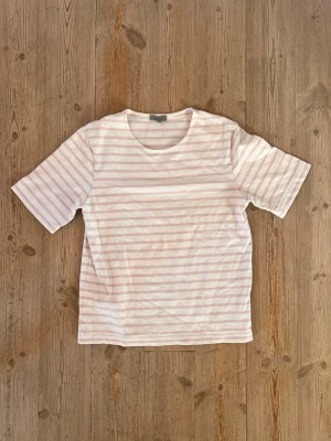 Randig t-shirt från COS i bomull - Säljer en fräsch vit t-shirt från COS med ljusrosa horisontella ränder. Klassisk rund halsringning och korta ärmar. 