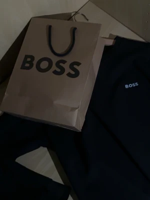 Svart sweatshirt från BOSS - Svart sweatshirt från BOSS med rund halsringning och diskret BOSS-logga broderad på bröstet. Storlek M men passar S. Tröjan har en klassisk passform och är perfekt för en stilren och avslappnad look. Materialet är mjukt och bekvämt. Pris kan diskuteras.