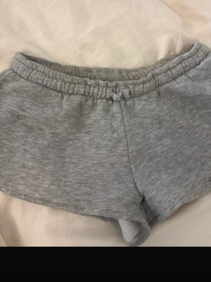 Grå mjukisshorts från Nelly - Mysiga grå mjukisshorts från Nelly med elastisk midja och snörning. Perfekta för chill dagar eller sommarhäng. Tillverkade i mjukt material som känns skönt mot huden.