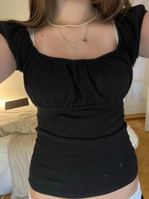 Svart topp med puffärmar - Säljer en svart topp med puffiga korta ärmar och rundad halsringning. Toppen har en figurnära passform och är tillverkad i ett mjukt material som känns bekvämt mot huden. Perfekt att styla med jeans eller kjol för en trendig look.