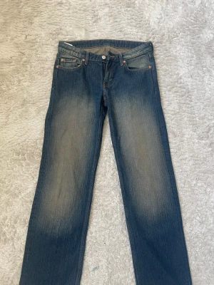 Blå raka lågmidjade jeans från weekday - Säljer ett par klassiska blå jeans med raka ben och en snygg gulaktig wash på låren och bakdelen.  Materialet är denim i bomull och passformen är avslappnad. Hon som har på dig jeansen är 165cm och har vanligtvis xs-s i jeans. Jeansen är i superskick utöver små slitningar längst ner (se bild 4 & 5).