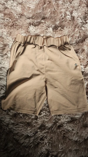 Beige shorts från ZINK - Säljer ett par snygga beige shorts från ZINK med hög midja och elastisk midjeresår. De har en enkel och clean design med sidofickor och mjukt material som känns skönt mot huden. Perfekta för varma dagar och chill outfits.