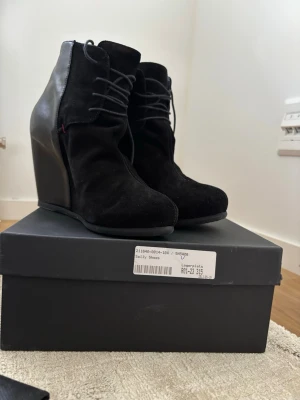 Costume National heels - Snygga svarta stövletter med kilklack och snörning framtill. Ovandelen är i mocka och baksidan i slätt skinnliknande material. Skorna har en modern siluett och passar perfekt till dig som vill ha både höjd och stil.