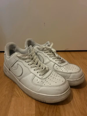 Nike air force - Säljer ett par vita sneakers i läder med perforerad tå, platt sula och snörning. Skorna har en enkel och stilren design med diskreta detaljer och passar perfekt till streetwear. Swoosh-logga på sidan och metallbricka vid snörningen.