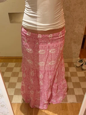 Rosa långkjol med vitt mönster - Säljer en rosa långkjol med vitt mönster. Kjolen har resår i midjan och är tillverkad i ett lätt och luftigt material, perfekt för varmare dagar🌸💗