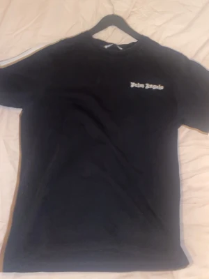 Svart Palm Angels t-shirt - Svart t-shirt från Palm Angels med klassisk passform och rund hals. Tryckt Palm Angels-logga i vitt på bröstet. Perfekt för en stilren och trendig look. Materialet känns mjukt och bekvämt mot huden.