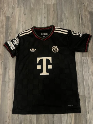 Olise tröja  - Snygg svart Bayern München matchtröja från Adidas med vita detaljer och röda inslag vid krage och ärmslut. Tröjan har klubbmärke, Adidas-logga och sponsortryck fram samt namn och nummer 'Olise 17' på ryggen. Tillverkad i lätt och ventilerande material.