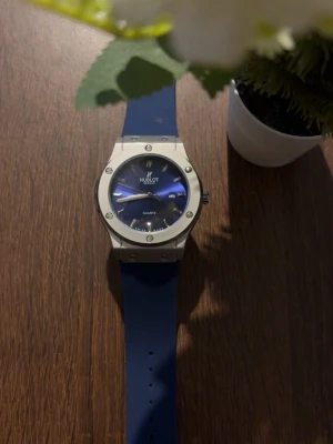 Klocka  - Snygg klocka med robust boett i silverfärgad metall och urtavla i blått respektive grönt. Klockan har datumvisning och matchande silikonarmband som ger en modern look. Perfekt accessoar för dig som gillar stilrena detaljer och exklusiv känsla.