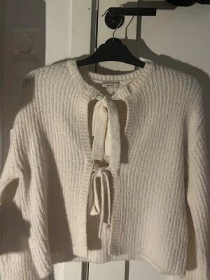 Vit stickad kofta från Gina Tricot - Mysig vit stickad kofta från Gina Tricot med ribbad struktur och två knytband framtill. Koftan har rund halsringning och långa ärmar, perfekt för lager-på-lager-stil. Materialet känns mjukt och fluffigt. Använd 3-4 gånger❤️