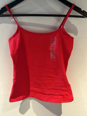 Rött linne med smala axelband - Säljer en enkel och snygg röd linnetopp i storlek XS. Toppen har smala axelband och ärmlös design, perfekt för varma dagar. Tillverkad i mjukt bomullsmaterial som känns skönt mot huden. Passar till jeans, kjol eller shorts. Såå fint linne men har redan ett exakt likadant, aldrig använt ❤️