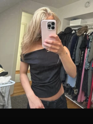 Svart offshoulder topp - Snygg svart offshoulder topp med asymmetrisk skärning och croppad passform. Toppen har en stilren look och är perfekt för dig som gillar trendiga detaljer. Materialet känns mjukt och följsamt mot kroppen.