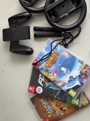 Nintendo Switch rattar och Joy-Con grepp - Två svarta rattar och ett svart Joy-Con grepp till Nintendo Switch. Perfekt för racing- och partyspel, tillverkade i slitstark plast. Inkluderar även två Joy-Con handledsremmar för extra säkerhet under spelandet.