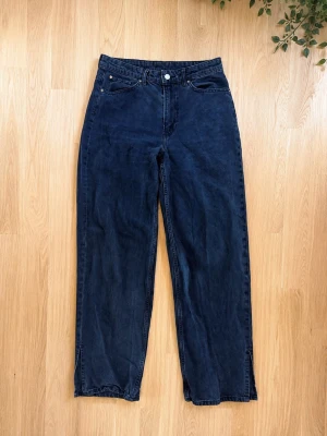Mörka raka jeans - Säljer ett par mörka jeans med rak passform och hög midja. Klassisk femficksmodell med knapp och dragkedja framtill. Jeansen har en enkel och tidlös look, perfekta till vardagsstilen. Materialet är denim i bomull. Finns slits vid benen