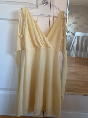 Ljusgul omlottklänning med v-ringning - Söt ljusgul kortklänning med omlott och djup v-ringning. Klänningen har långa, luftiga ärmar och är tillverkad i ett tunt, lätt material som passar perfekt till varmare dagar. Stilren och enkel design som ger en fräsch look.