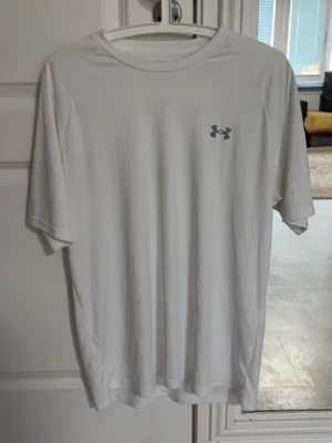 Under Armour T-shirt  - Vit Under Armour T-shirt i polyester perfekt för träning och vardagen. Tröjan har några små slitna delar med hål som visas i fjärde bilden men är väldigt små och knappt märkbara. Storlek Large
