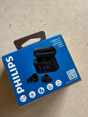 Philips T6000 trådlösa in-ear hörlurar - Säljer ett par helt nya oanvända svarta trådlösa in-ear hörlurar från Philips, modell T6000. Hörlurarna har aktiv brusreducering, upp till 28 timmars batteritid och laddas i ett smidigt etui med digital display. Vattentåliga enligt IPX5 och har mikrofon för samtal.