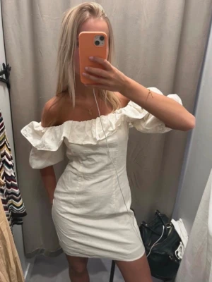 Vit offshoulder kortklänning - Supersöt vit kortklänning från h&m med offshoulder och volangdetaljer längs axlarna. Klänningen har en figurnära passform och är tillverkad i ett lätt tyg, perfekt för varma dagar. Puffiga ärmar ger en trendig touch och den stilrena looken passar till många tillfällen. Använd 1 gång. Slutsåld! 🤍