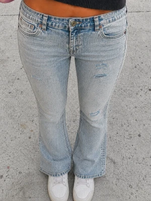 Ljusblå bootcut jeans med slitningar - Säljer ett par ljusblå bootcut jeans med slitna detaljer och klassisk femficksmodell. Jeansen har en något utsvängd passform nedtill och är tillverkade i denim med en snygg tvätt. Perfekta för en avslappnad och trendig look.