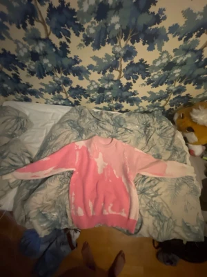 Rosa och vit batikstickad tröja - Unik stickad tröja i batikstil med rosa och vita nyanser. Tröjan har rund halsringning, långa ärmar och avslappnad passform. Perfekt för dig som vill sticka ut med en färgglad och trendig look.