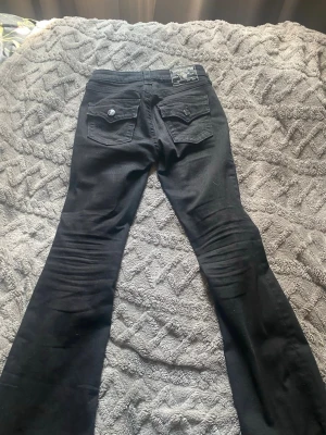 Svarta True Religion  bootcut, UPPSYDDA är på gränsen för kort till mig som är 160🤍 - Snygga svarta jeans från True Religion med bootcut-modell och detaljerade fickor bak med lock och knappar. Klassisk patch på linningen. Perfekta för dig som vill ha en cool och tidlös look.