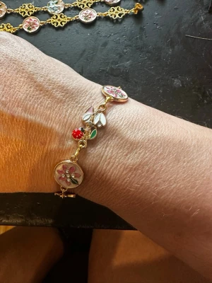 Guldigt armband med blommor och pärlor - Unikt armband i guldfärg med runda länkar dekorerade med blommor 