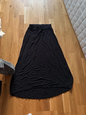 Svart långkjol i mjukt tyg - En svart långkjol med enkel design och mjukt, följsamt tyg. Kjolen har en bred resår i midjan och faller snyggt längs benen. Perfekt för dig som gillar en stilren och bekväm look.