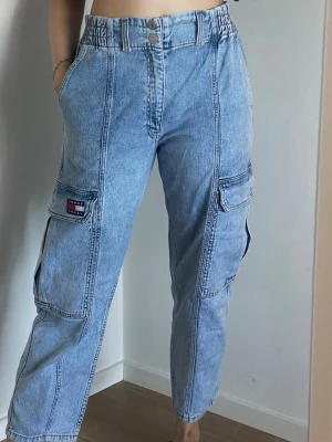 Tommy Jeans cargo jeans ljusblå W31/L32 - Ljusblå cargo jeans från Tommy Jeans i storlek W31/L32. Relaxed fit med hög midja, sidofickor och fina Tommy-detaljer. Använda men i väldigt fint skick. Material: 99% bomull, 1% elastan.