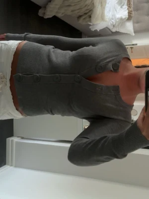 H&M - Snygg grå kofta från H&M med rund halsringning och stora knappar framtill. Modellen är figurnära med långa ärmar och ribbade muddar vid ärmslut och nederkant. Perfekt att slänga över en topp för en chill look.
