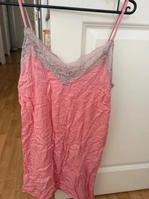 Rosa nattlinne med spetsdetaljer - Sött nattlinne i rosa med tunna axelband och vacker ljuslila spets längs urringningen. Materialet är mjukt och lätt, perfekt för att chilla hemma eller sova i. Bara legat i garderoben. Storlek S😊.