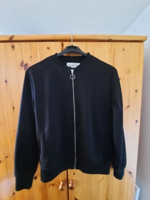 Svart ziptröja med rund hals - Svart ziptröja med rund halsringning och hel dragkedja framtill. I lappen står det att den är storlek S, men den passar mig som brukar använda M/L i överdelar. Jag gissar att den sitter lite "oversized" för mindre storlekar.
