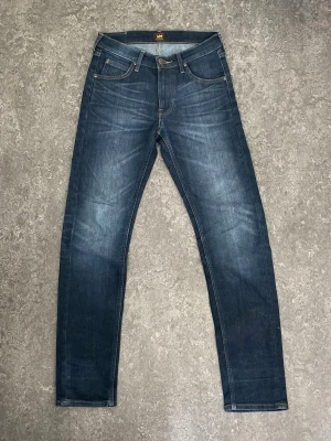 Mörkblå Lee jeans  - Mitt pris 200kr nya 1400kr . Snygga mörkblå jeans från Lee med klassisk femficksdesign och raka ben. Jeansen har kontrastsömmar, läderpatch med Lee-logga bak och är tillverkade i slitstarkt denim. Perfekt passform med normal midja och straight fit.