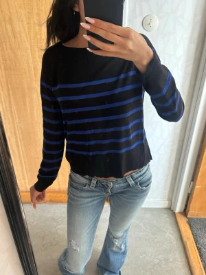 Svart tröja med blå ränder - Snygg svart långärmad tröja med blå ränder från ZARA. Tröjan har ett litet hål vid axeln. 
