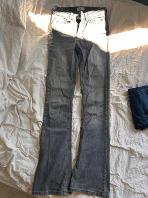 Grå bootcut jeans från ONLY - Säljer ett par grå bootcut jeans från ONLY med klassisk femficksmodell och dragkedja. Jeansen har en lätt tvättad look och utsvängda ben. Jeansen är högmidjade.