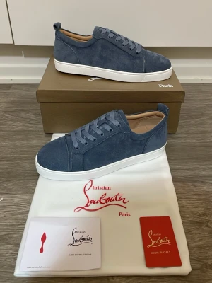 Christian Louboutin skor blå - Snygga blå sneakers i mocka från Christian Louboutin med klassisk låg profil och vita sulor. Skorna har matchande blå skosnören och diskreta sömmar för en clean look. Perfekta för dig som vill ha något stilrent och exklusivt i garderoben.