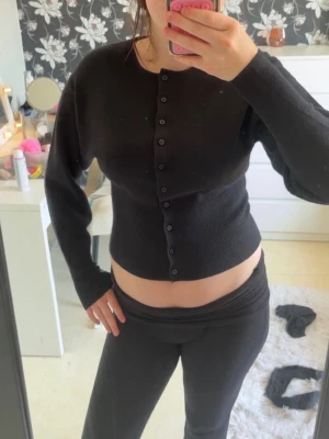 Svart ribbad kofta med knappar - Säljer en svart ribbad kofta med långa ärmar och rund halsringning. Koftan har knäppning hela vägen framtill och en figurnära passform. Perfekt att styla med både jeans och kjol för en clean look. Den är som ny, har bara använt den 1 gång! Den är storlek M men känns som S